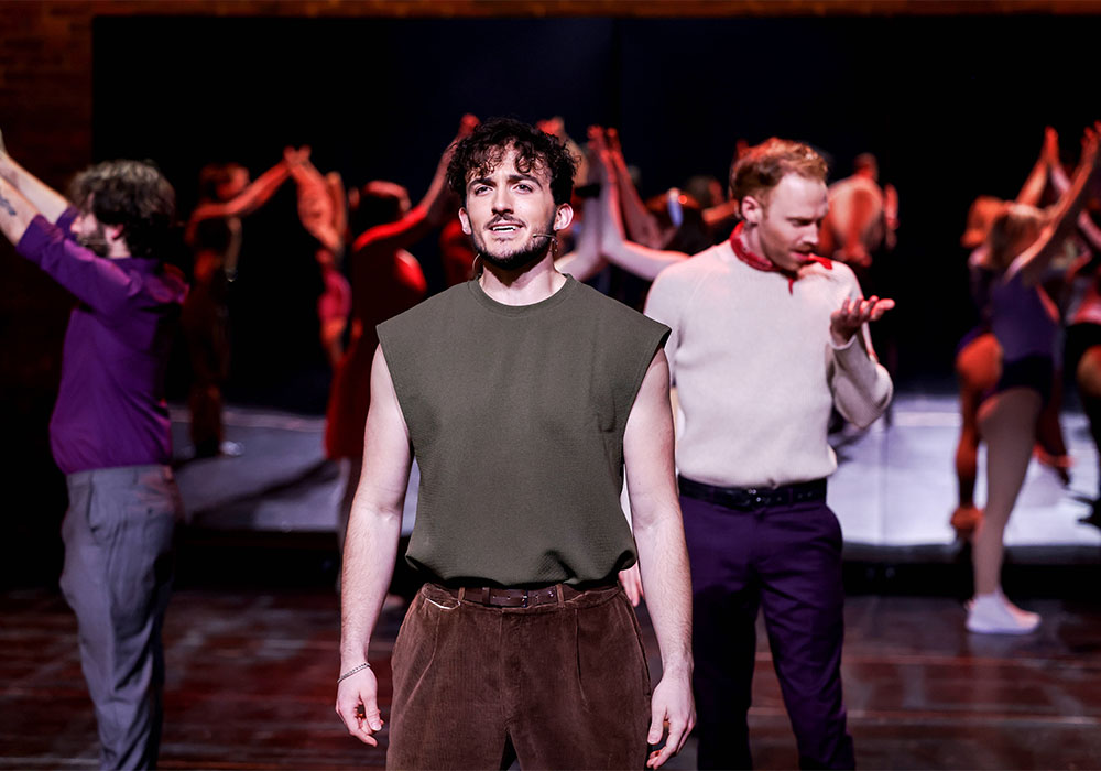 A performer sings solo centre stage in a sleeveless top while the ensemble dances behind him, A Chorus Line, National Theatre St Kilda.